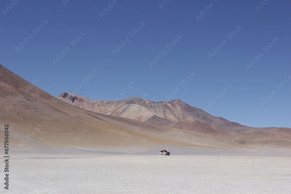 Solitary Vehicle in Bolivian Desert. Remote desert landscape in Bolivia with a solitary vehicle under a bright blue sky. Solitary Vehicle in Bolivian Desert. Remote desert landscape in Bolivia with a solitary vehicle under a bright blue sky.