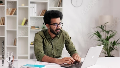 Satisfied Indian man in black glasses checking his email and happy with good news. A young man winner celebrating the victory, raises his hands uphill.