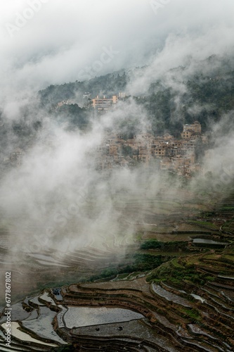 Vertical shot of the rice terraces with a town hiding behind a cloud