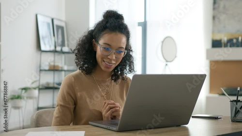 Portrait of happy multi ethnical woman looking at laptop screen indoors. Elegant businesswoman in glasses chatting online. Positive young business woman using computer for online interview or training photo