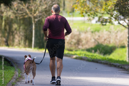 A man have jogging in park with dog on a leash