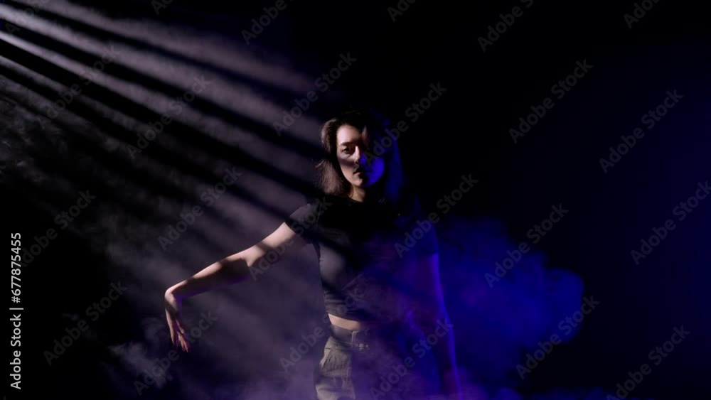 Attractive woman dancing jazz funk in studio filled with smoke, rays of light on blue neon, black background. Attractive woman dancing jazz funk in studio filled with smoke, rays of light on blue neon, black background.