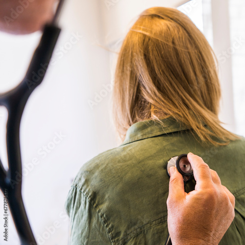 Doctor using stethoscope on his patient's back to listening to lungs for breathing problem.