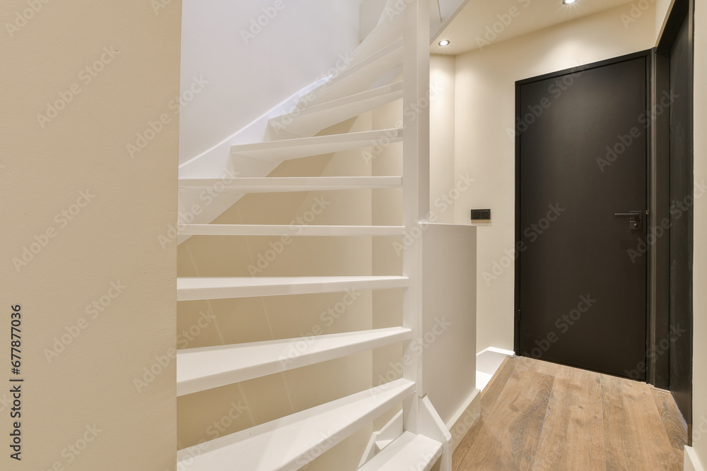 a room with some stairs and a black door in the corner to the right is a white staircase leading up a room with some stairs and a black door in the corner to the right is a white staircase leading up