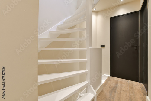 a room with some stairs and a black door in the corner to the right is a white staircase leading up