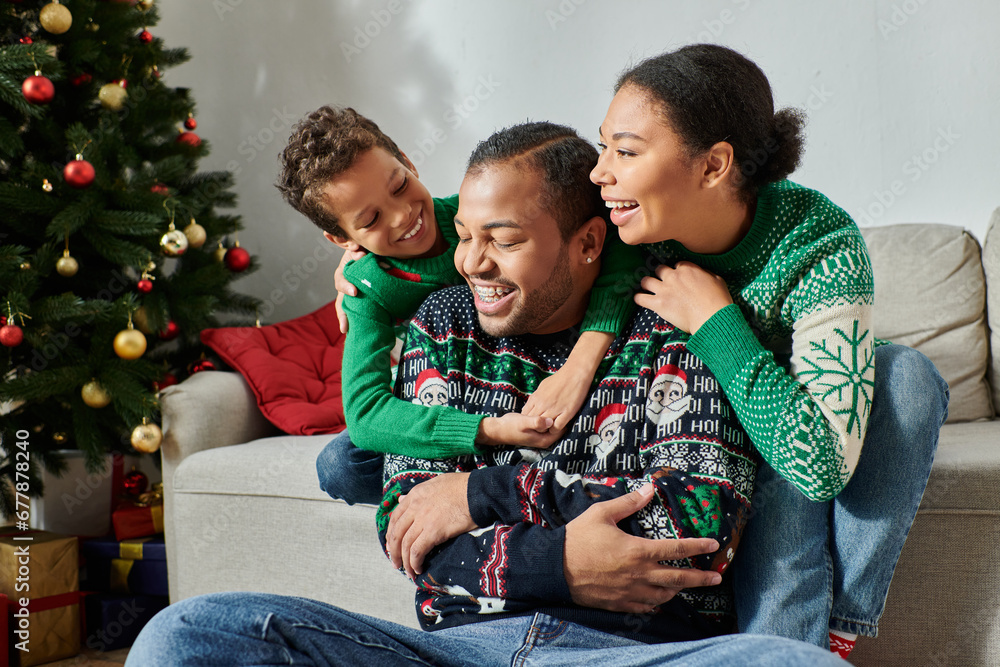 happy african american family in cozy sweaters hugging warmly and smiling joyfully, Christmas