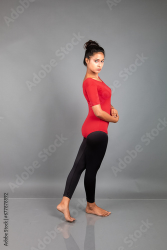 Healthy young woman in red t-shirt and black leggings doing yoga and stretching exercises isolated on grey background