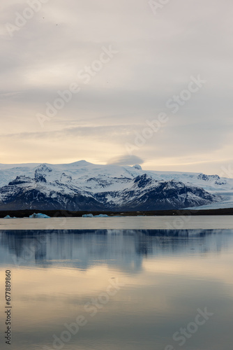 Icelandic frozen region with scandinavian style pond and mountains covered in snow. Polar adventure road across chilly paradise with spectacular sunset glow during golden hour.