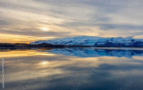 Lake and snowy mountains at sunset in iceland with majestic nordic landscape, freezing cold water. Scandinavian roadside scenery with hills during golden hour, wonderland scenic route.
