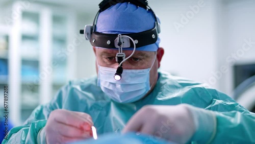 Concentrated look of a male surgeon with headlight. Portrait of a doctor using tools at otolaryngologic operation. photo