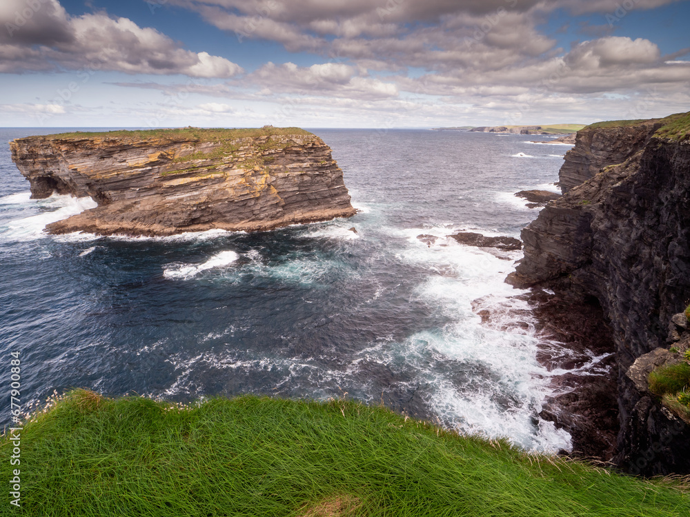 View on rough small island in the ocean from a cliff, Ireland, Kilkee area. Warm sunny day, blue cloudy sky. Travel, tourism and sightseeing concept. Irish landscape and coastline. View on rough small island in the ocean from a cliff, Ireland, Kilkee area. Warm sunny day, blue cloudy sky. Travel, tourism and sightseeing concept. Irish landscape and coastline.