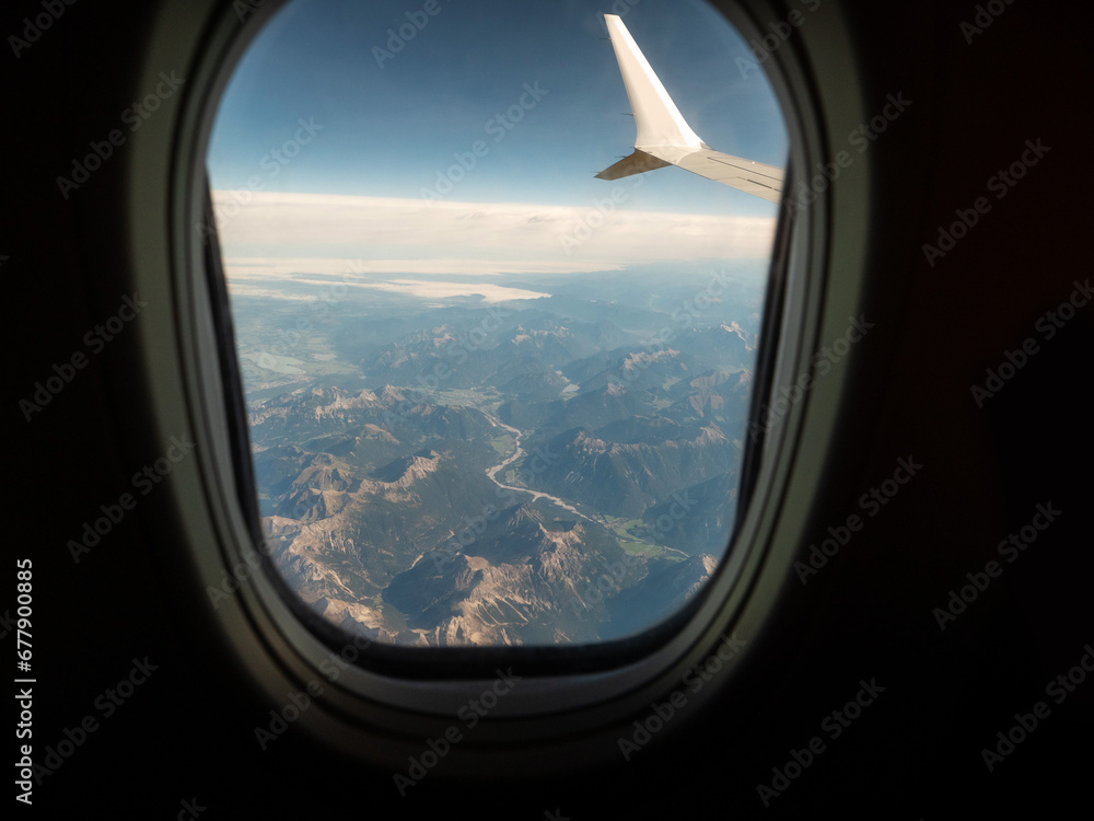 View from an airplane window of a mountain area and left wing, warm sunny day. Travel and tourism view. Flying to holiday destination point. Scene through illuminator. High viewpoint. View from an airplane window of a mountain area and left wing, warm sunny day. Travel and tourism view. Flying to holiday destination point. Scene through illuminator. High viewpoint.