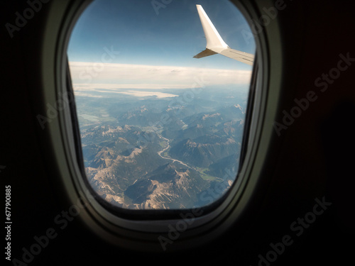 View from an airplane window of a mountain area and left wing, warm sunny day. Travel and tourism view. Flying to holiday destination point. Scene through illuminator. High viewpoint.