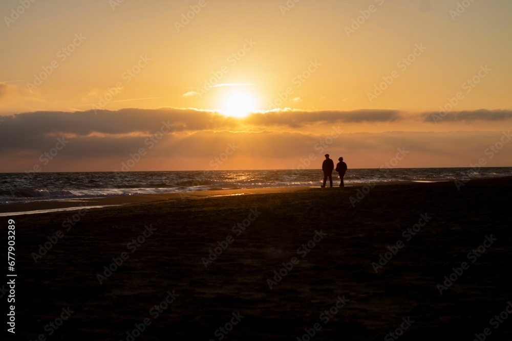 Silhouette view of a couple walking on the beach by the sea under orange sunset scene