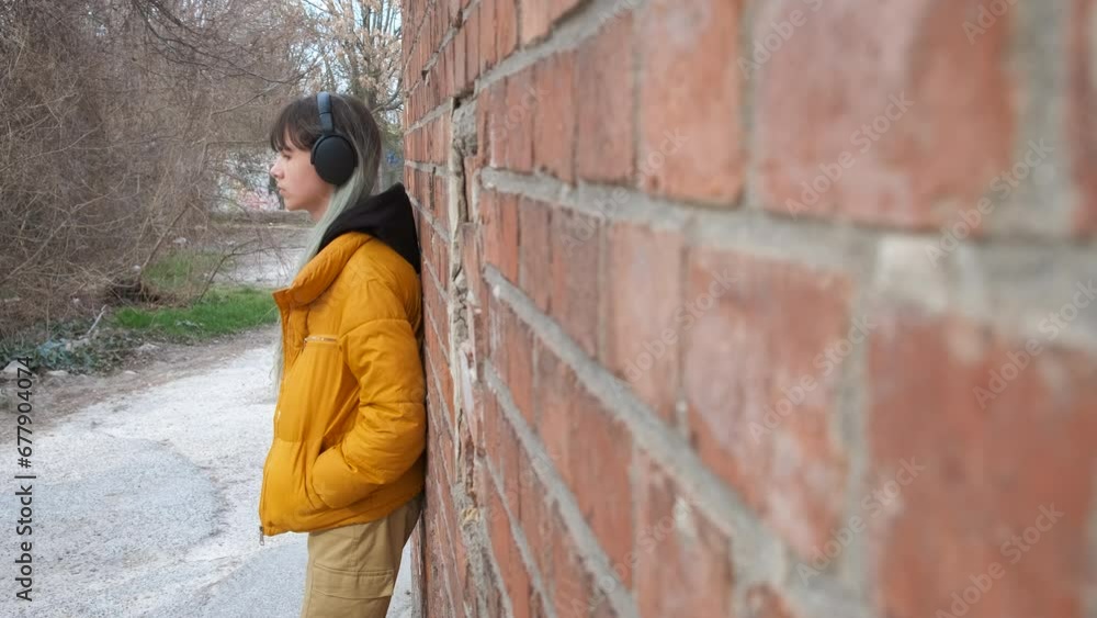 Teen stand alone in headphones by wall. A stylish teen girl learning by the wall and listen the music in headphones. Teen stand alone in headphones by wall. A stylish teen girl learning by the wall and listen the music in headphones.