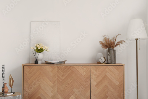 Wooden cabinet with alarm clock, tulip flowers and reed diffuser near white wall photo