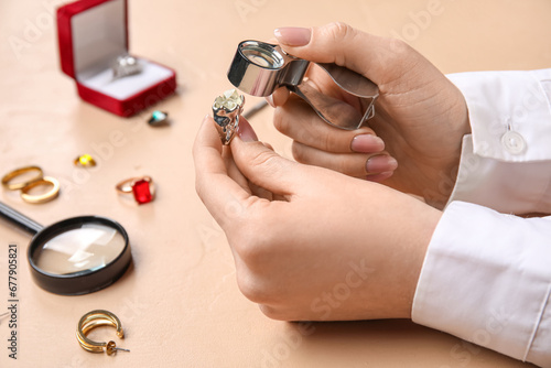 Female jeweler examining ring on beige table, closeup