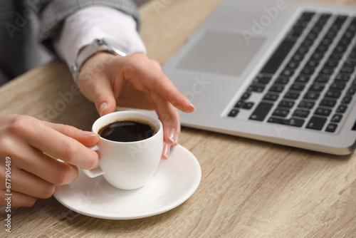 Woman holding cup of coffee at table with modern laptop