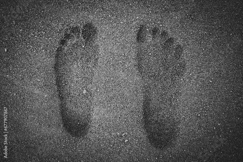 Black and white human barefoot footprints in wet, black volcanic sand of a beach. 