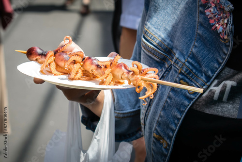 A woman holding a plate of freshly cooked skewered tiny octopusses as a street food snack in Tsukiji Fish Market, Tokyo, Japan.  photo