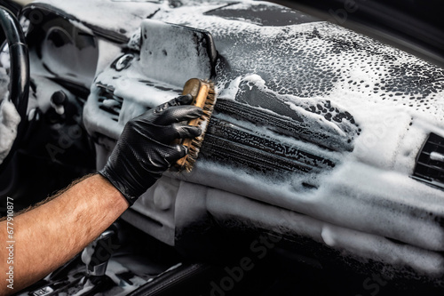 A mechanic cleans the interior of a car with a brush and foam.