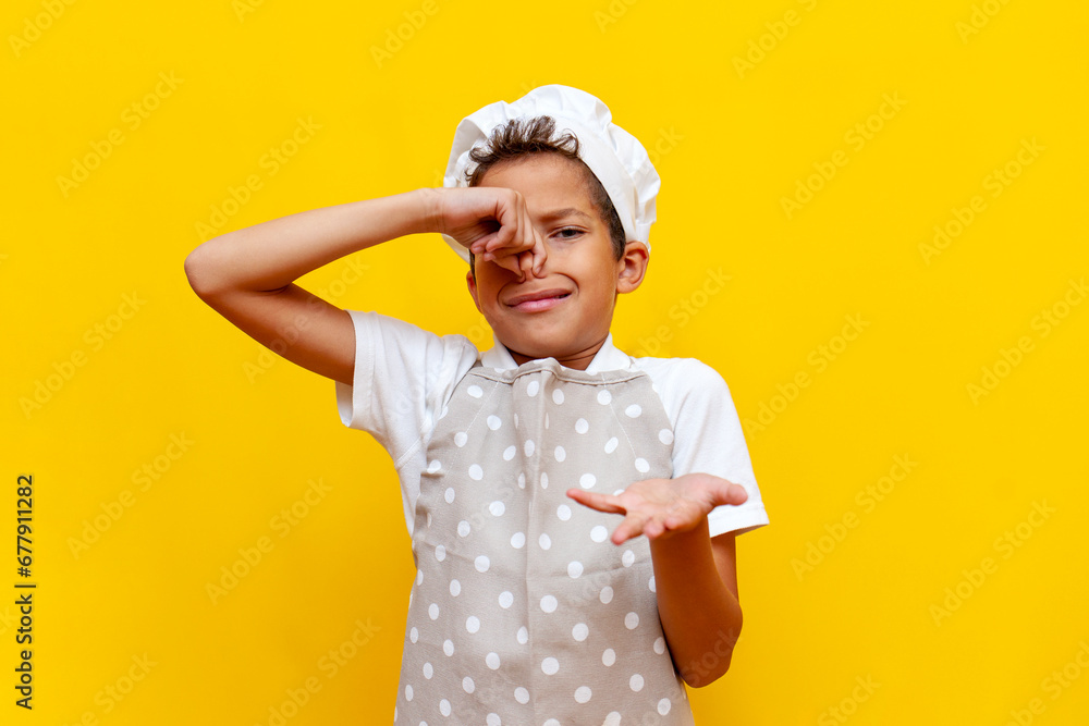african american boy in uniform and chef's hat covers his nose with his hand and avoids the bad smell - obrazy, fototapety, plakaty 