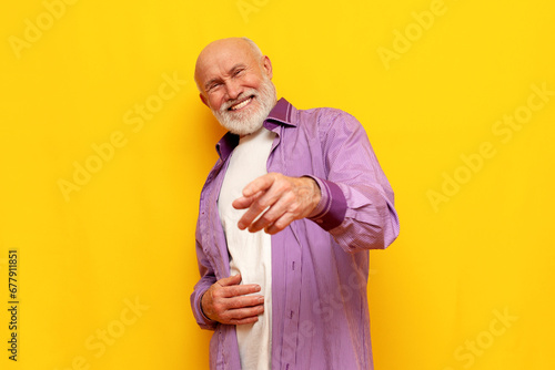 old bald grandfather with gray beard points forward and laughs on yellow isolated background photo