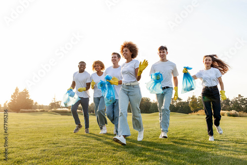 multiracial group of people running to clean the park from garbage and plastic with gloves and garbage bags