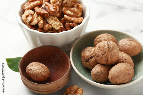 Bowls of tasty walnuts on white marble background