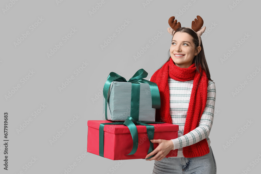 Beautiful young woman in reindeer horns with gift boxes on grey background Beautiful young woman in reindeer horns with gift boxes on grey background