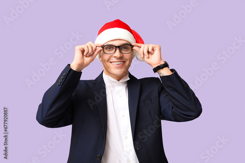 Young businessman in Santa hat on purple background