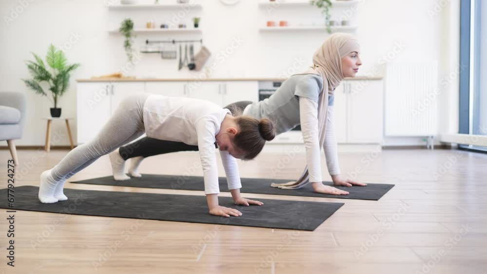 Attractive muslim mother in hijab practicing plank position with baby daughter in kitchen after wake up in morning. Feeling so comfortable and relax. Yoga of woman with her baby girl for healthcare. Attractive muslim mother in hijab practicing plank position with baby daughter in kitchen after wake up in morning. Feeling so comfortable and relax. Yoga of woman with her baby girl for healthcare.