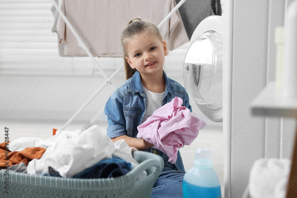 Little girl putting dirty clothes into washing machine in bathroom Little girl putting dirty clothes into washing machine in bathroom