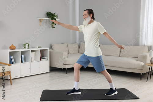 Fototapeta Naklejka Na Ścianę i Meble -  Senior man in sportswear doing exercises at home