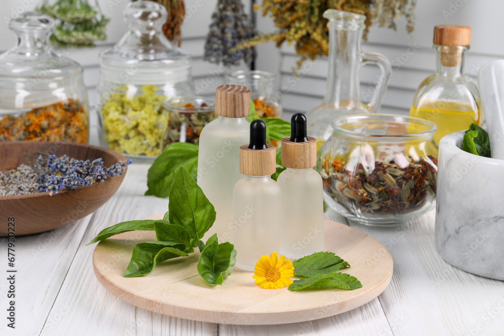 Bottles of essential oils, leaves, flower and herbs on white wooden table Bottles of essential oils, leaves, flower and herbs on white wooden table