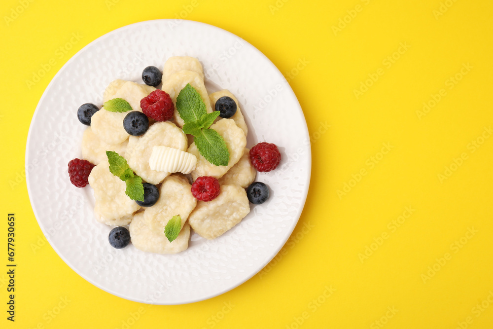 Plate of tasty lazy dumplings with berries, butter and mint leaves on yellow background, top view. Space for text Plate of tasty lazy dumplings with berries, butter and mint leaves on yellow background, top view. Space for text