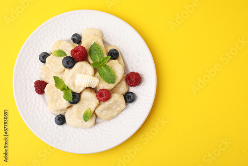 Plate of tasty lazy dumplings with berries  butter and mint leaves on yellow background  top view. Space for text