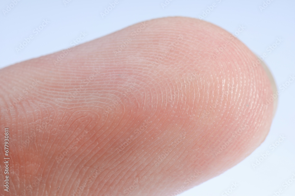Finger with friction ridges on light blue background, macro view Finger with friction ridges on light blue background, macro view
