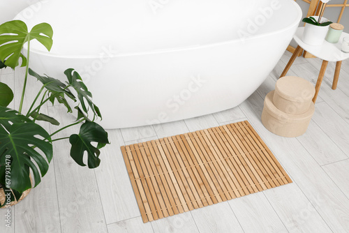 Stylish bathroom interior with bath tub, houseplant and bamboo mat