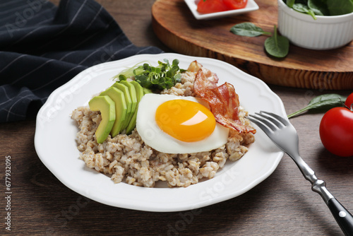 Tasty boiled oatmeal with fried egg, avocado and bacon served on wooden table