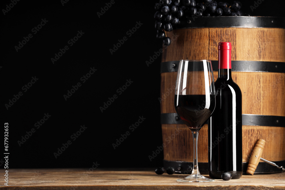 Delicious wine, wooden barrel and ripe grapes on table against black background. Space for text