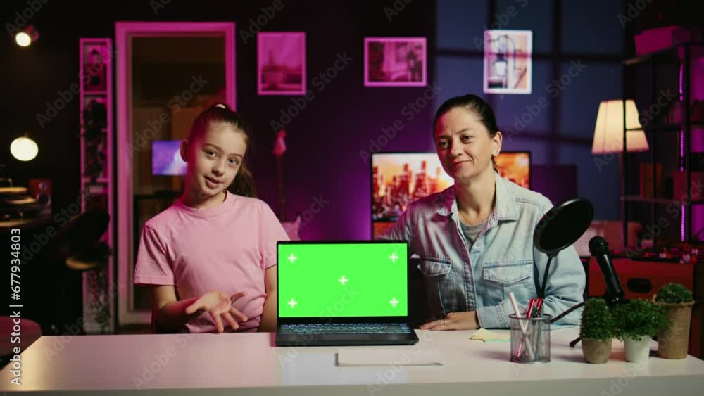 Happy child and her loving mom recording green screen laptop review on online platforms. Young smiling daughter and parent presenting mockup notebook, filming in home studio with pink neon lighting Happy child and her loving mom recording green screen laptop review on online platforms. Young smiling daughter and parent presenting mockup notebook, filming in home studio with pink neon lighting