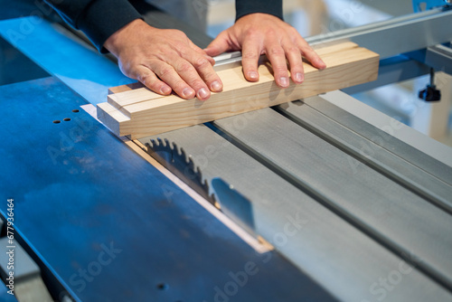Closeup shot, man cutting peace of wood on a industrial table saw  photo