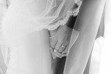 A black and white portrait of a bride and groom holding hands underneath a lace veil on their wedding day