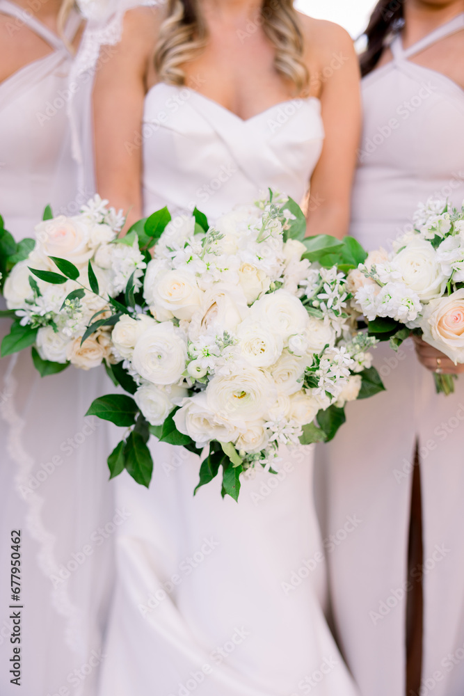 Bride in a wedding dress is standing next to her bridesmaids holding a classic white spring wedding flower bouquets. Bride in a wedding dress is standing next to her bridesmaids holding a classic white spring wedding flower bouquets.