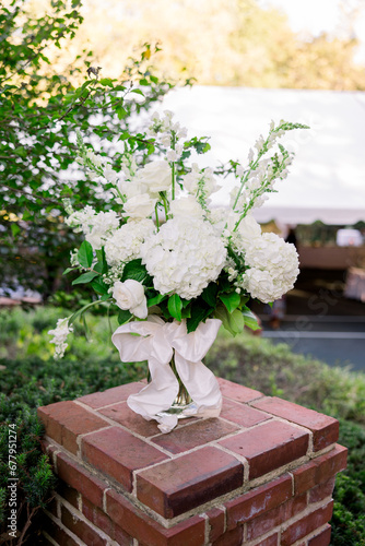 A beautiful vase of white flowers and hydrangeas sitting on a brick column outside.