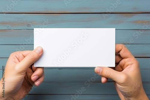 Hand holding white business card on blue wooden background. Top view.