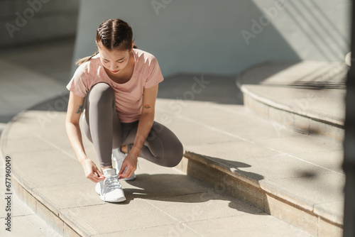 Young Asian woman tying shoelace on her running shoes. Preparation before jogging exercise. Fitness and sport activity. Healthy exercise concept. photo