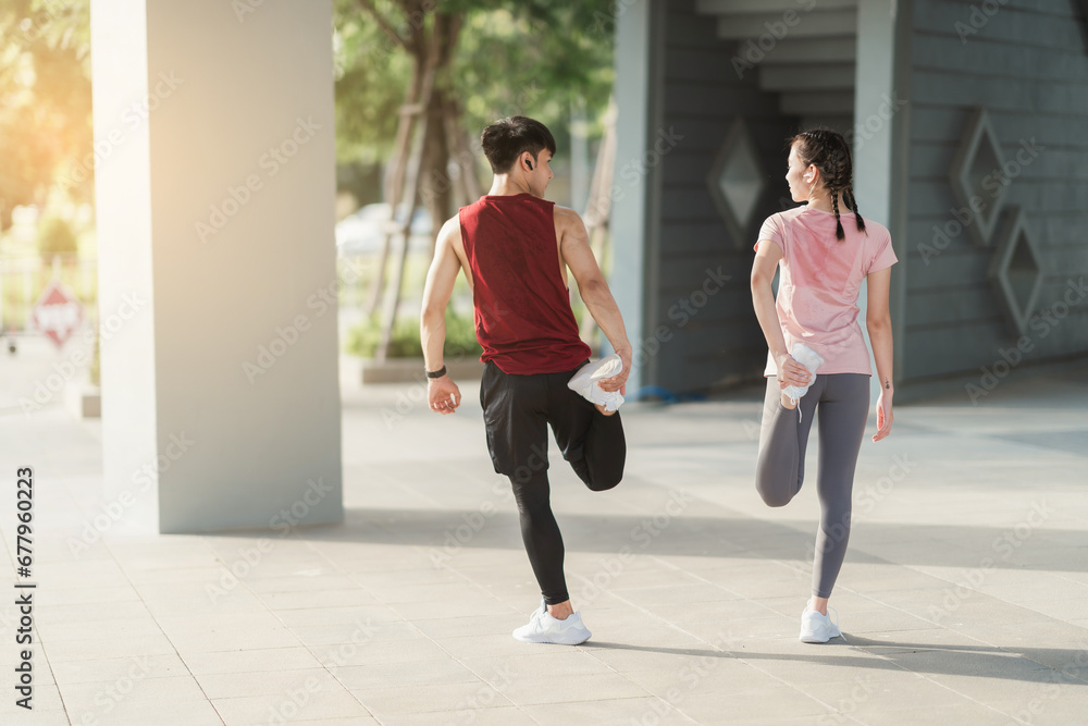 Young Asian couple in sportswear doing stretching together before jogging exercise in urban area. Warming up for workout outdoor in the morning.