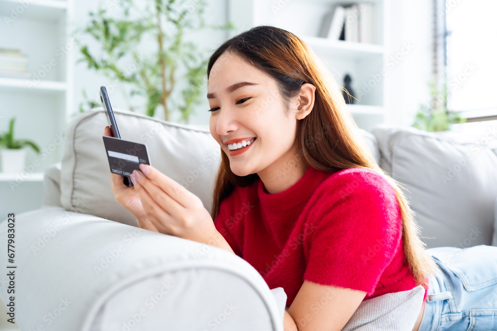 Young asian woman lying on sofa in living room, makes online banking payments through the internet from bank card on cell phone. Shopping online on mobile with credit card Young asian woman lying on sofa in living room, makes online banking payments through the internet from bank card on cell phone. Shopping online on mobile with credit card